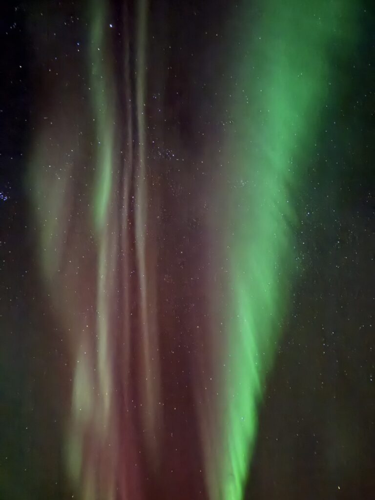 冰島夜空中舞動的極光，綠色與紫紅色光帶交織布滿星空，北歐極光攻略最震撼瞬間