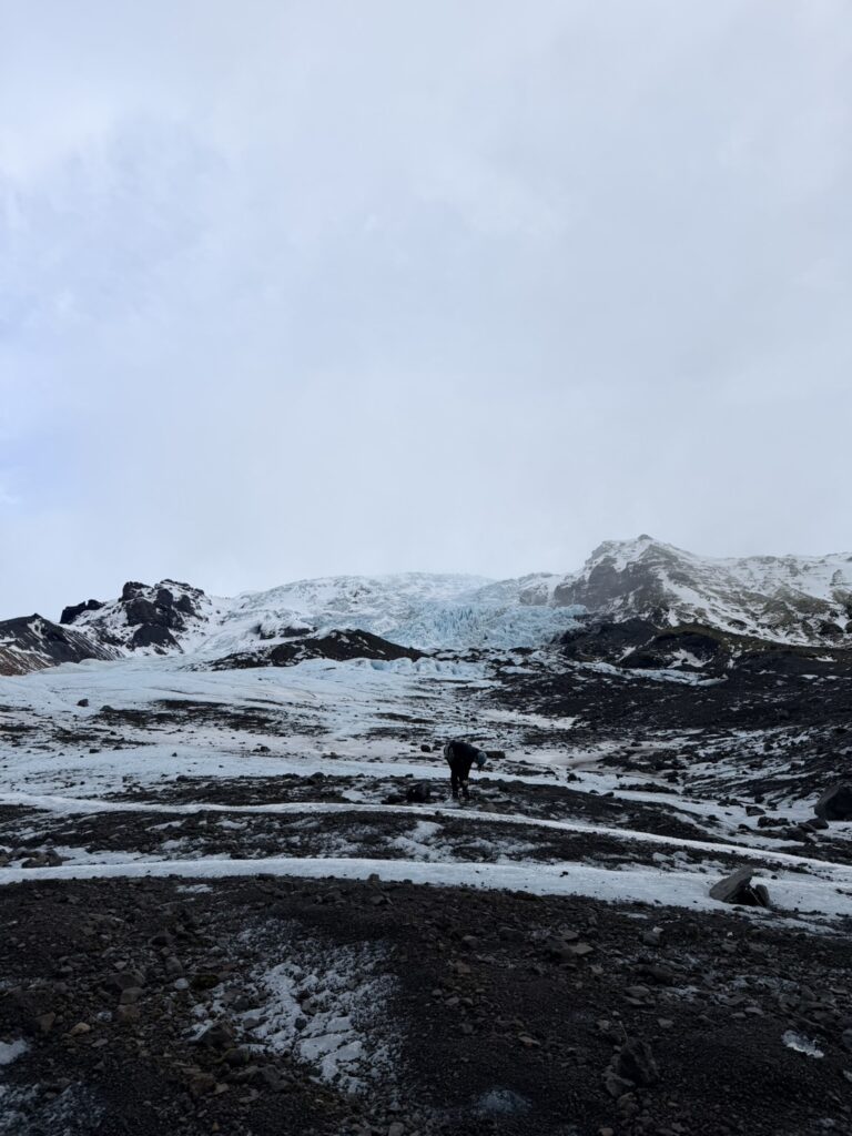 冰島自由行冰川健行，黑色火山岩地形與藍白冰川交錯，遠方雪山壯觀景色